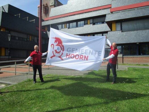 Burgemeester en wethouder hijsen vlag nieuw logo