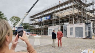 Het laatste dak-element wordt op het sport- en zorghuis gehesen. Op de voorgrond kijken wethouder René Assendelft en centrumdirecteur Leen Koole toe.