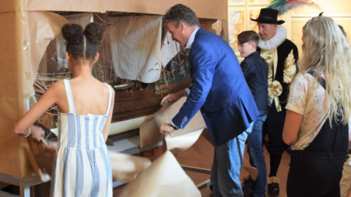 Wethouder Simon Broersma pakt samen met twee leerlingen uit groep 8 van basisschool Het Fluitschip het model van het fluitschip De Risdam  uit (Foto Henk Sas)