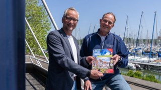 Foto Benno Ellerbroek - uitgever Ron Dol (l) overhandi eerste exemplaar van de stadsgids aan havenmeester Jos de Groot van de Grashaven.